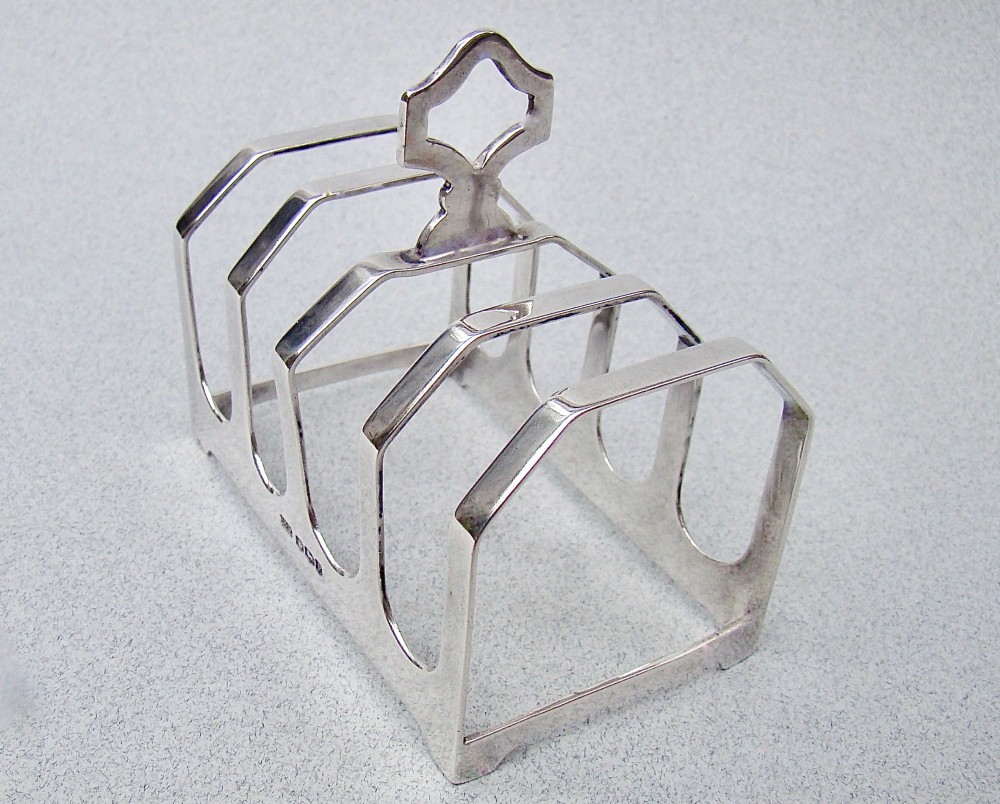 An Art Deco solid silver four-slice toast rack featuring angular dividers and a geometric central handle. View VI