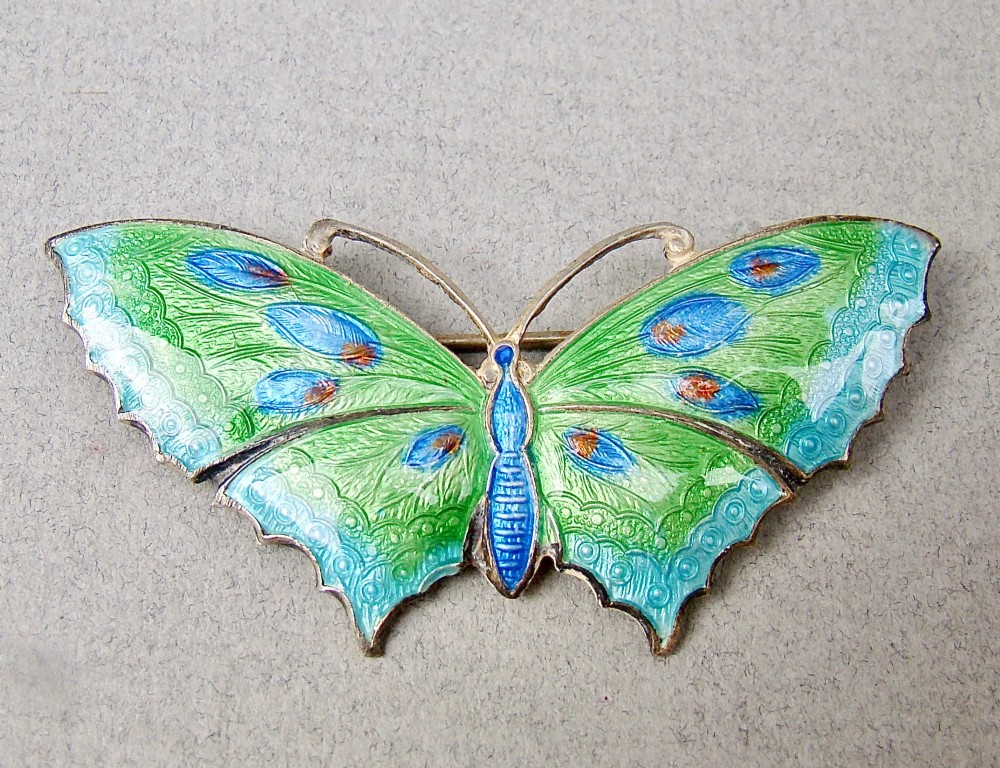 A butterfly brooch constructed from sterling silver featuring bright green, turquoise, and blue guilloche enamel across the wings and body.