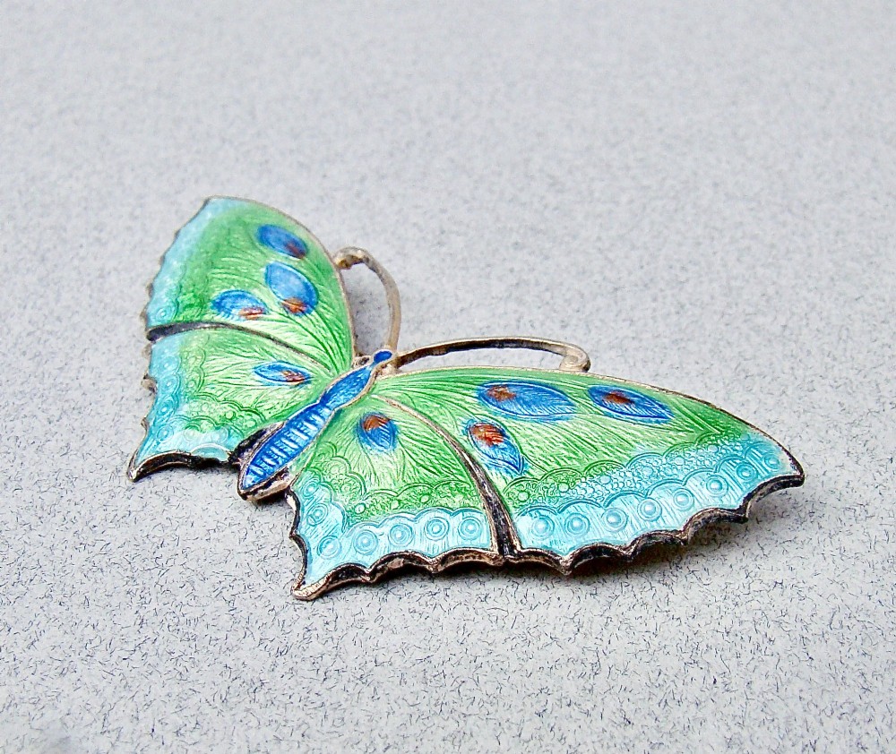 A butterfly brooch constructed from sterling silver featuring bright green, turquoise, and blue guilloche enamel across the wings and body. View II