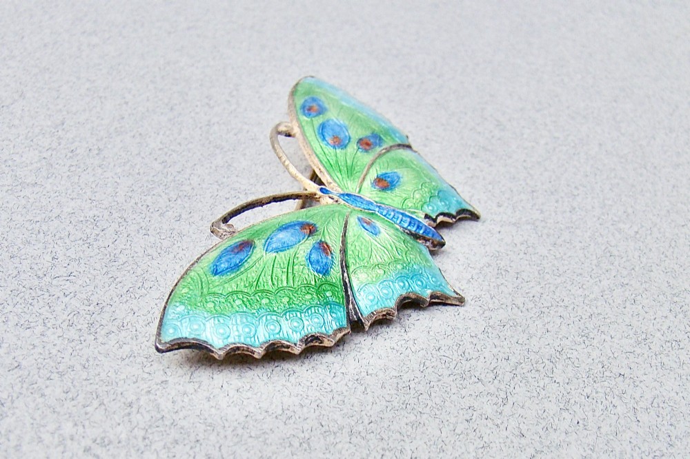A butterfly brooch constructed from sterling silver featuring bright green, turquoise, and blue guilloche enamel across the wings and body. View III