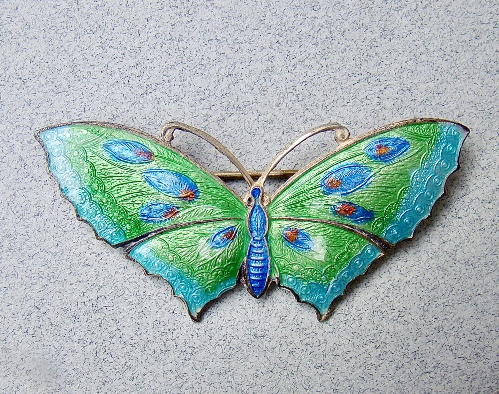 A butterfly brooch constructed from sterling silver featuring bright green, turquoise, and blue guilloche enamel across the wings and body. View V