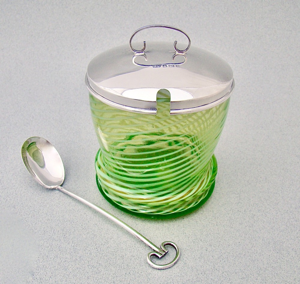 A green spiral-patterned vaseline glass preserve pot with a polished hallmarked silver lid and matching silver spoon.