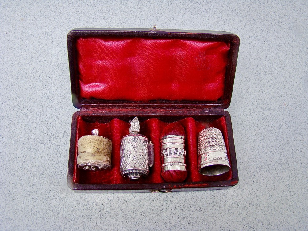 An open dark-cased Victorian sewing set lined with crimson red silk velvet, containing four decorated silver tools including a thimble, needle case, pin cushion, and waxer. View III
