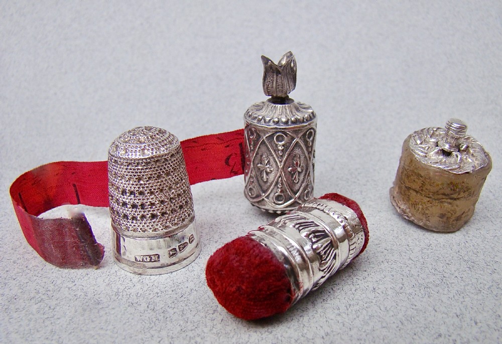 An open dark-cased Victorian sewing set lined with crimson red silk velvet, containing four decorated silver tools including a thimble, needle case, pin cushion, and waxer. View VI