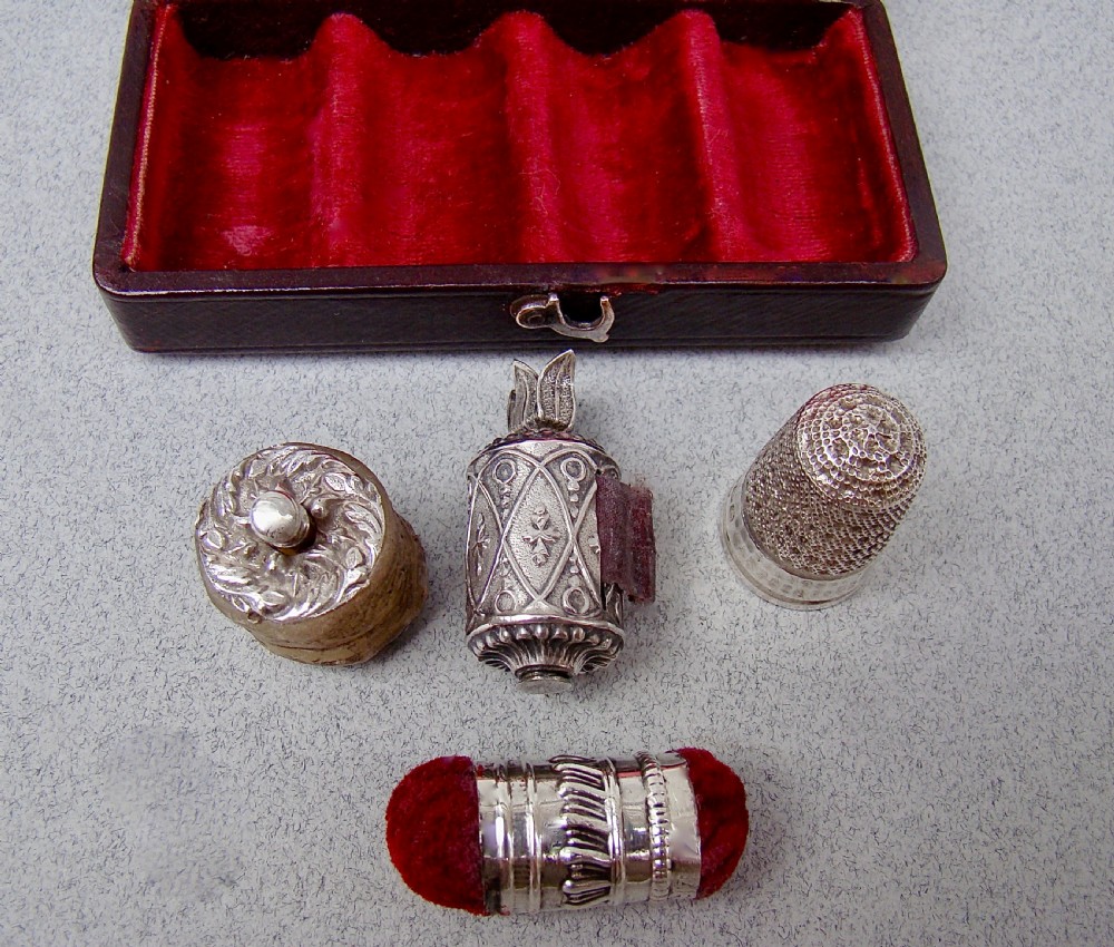 An open dark-cased Victorian sewing set lined with crimson red silk velvet, containing four decorated silver tools including a thimble, needle case, pin cushion, and waxer. View VII