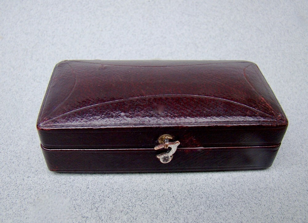 An open dark-cased Victorian sewing set lined with crimson red silk velvet, containing four decorated silver tools including a thimble, needle case, pin cushion, and waxer. View VIII