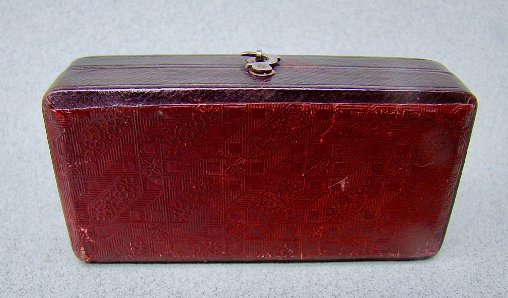 An open dark-cased Victorian sewing set lined with crimson red silk velvet, containing four decorated silver tools including a thimble, needle case, pin cushion, and waxer. View IX