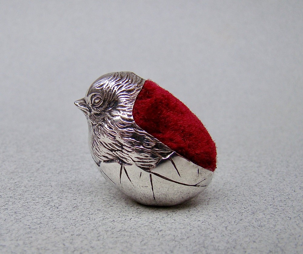 An Edwardian sterling silver pin cushion formed as a hatching chick emerging from an eggshell with a red velvet insert.