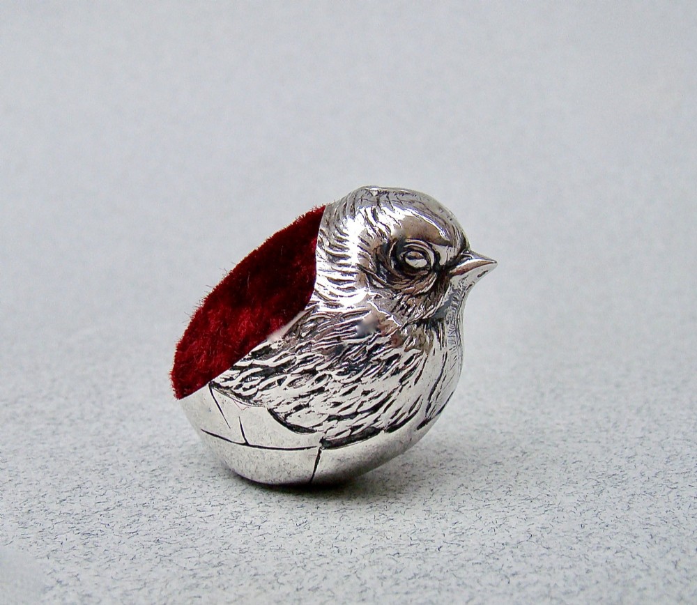 An Edwardian sterling silver pin cushion formed as a hatching chick emerging from an eggshell with a red velvet insert. View II