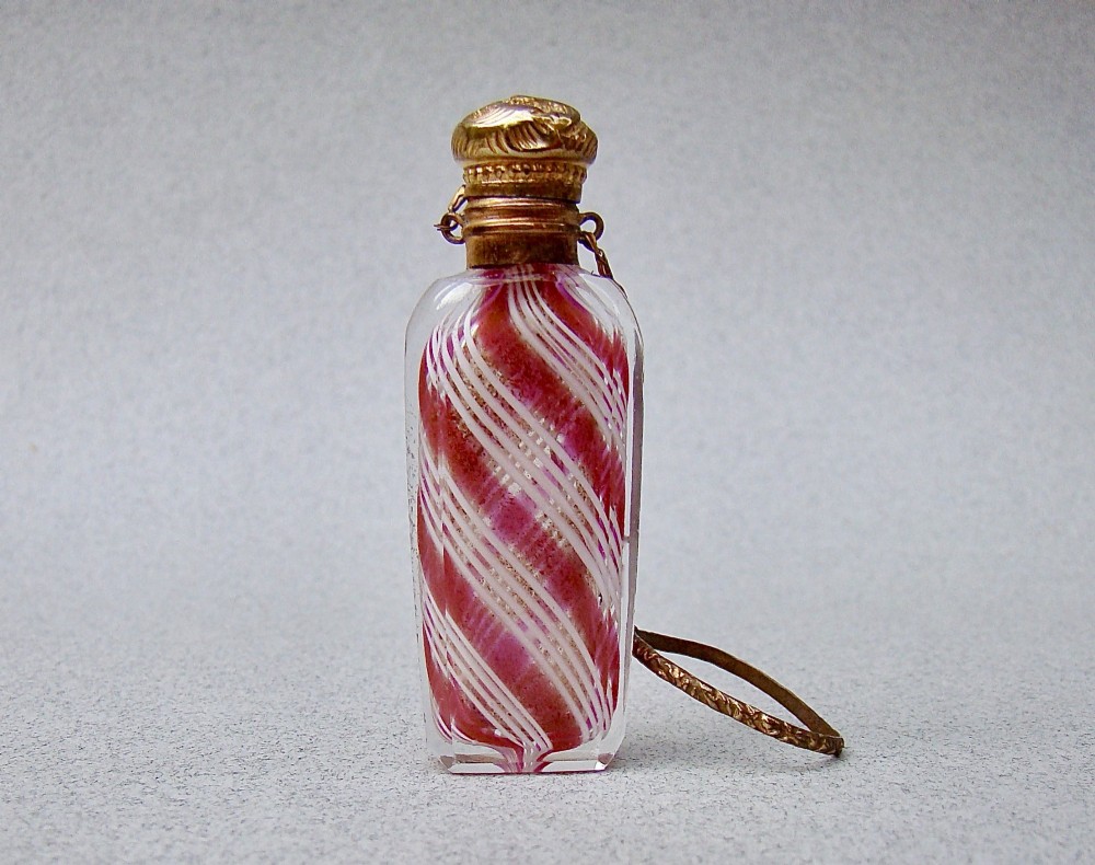 A miniature 19th-century French Clichy clear glass scent bottle featuring internal pink and white diagonal swirls, topped with an embossed gilt brass cap and suspension ring.