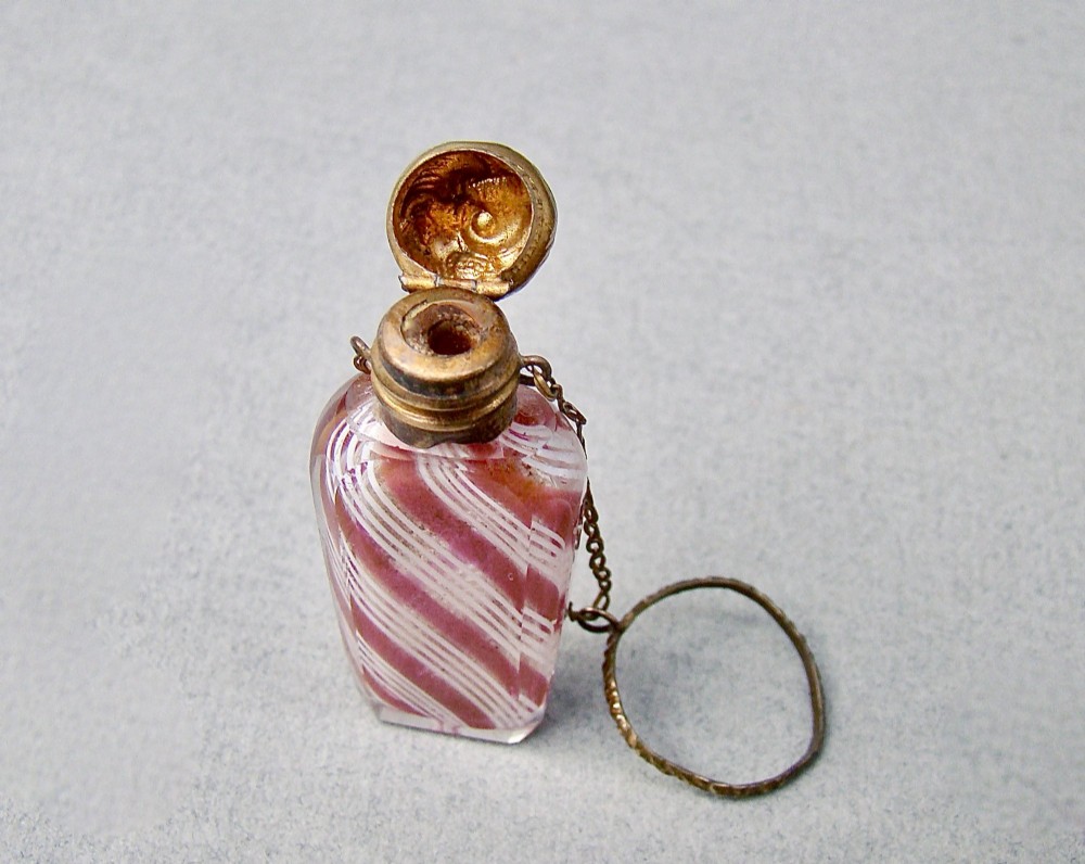 A miniature 19th-century French Clichy clear glass scent bottle featuring internal pink and white diagonal swirls, topped with an embossed gilt brass cap and suspension ring. View V