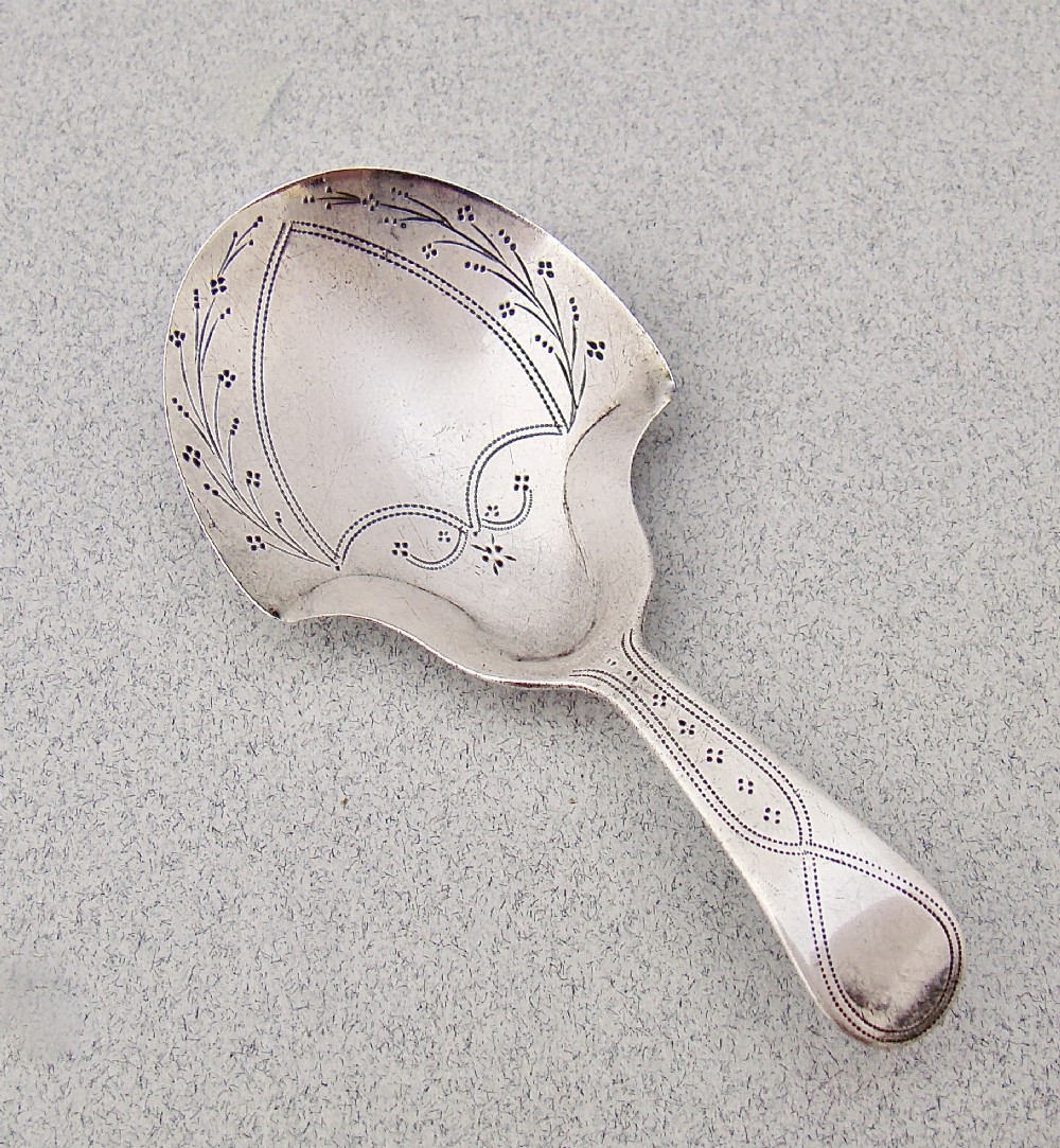 An eighteenth-century sterling silver caddy spoon featuring a spade-shaped bowl decorated with delicate bright-cut floral engraving and a short tapered handle.