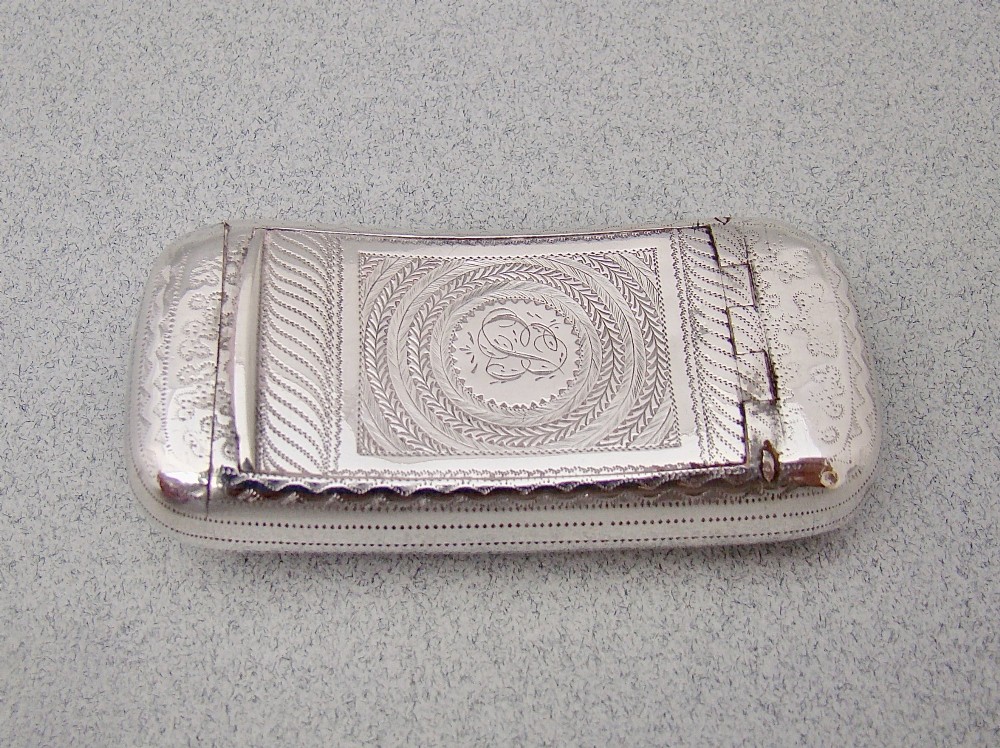 A rectangular Georgian sterling silver snuff box with a curved shape, engine-turned detail, and a central engraved monogram.