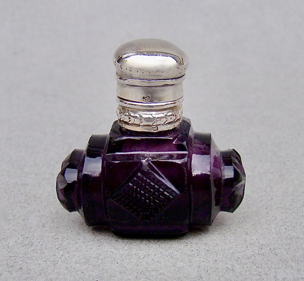 A miniature barrel-shaped purple amethyst cut glass scent bottle with a silver cap and collar.