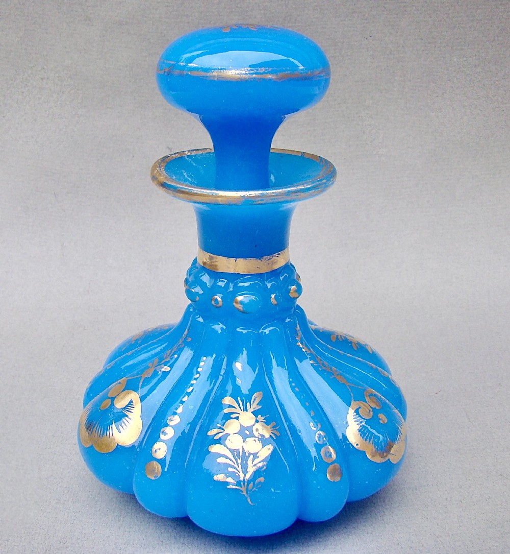 A bright blue lobed opaline glass scent bottle with a flared rim, ground glass stopper, and hand-gilded floral motifs.