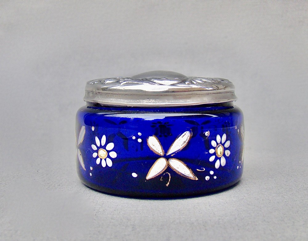 A small cylindrical cobalt blue glass jar decorated with white enamelled floral motifs and topped with an embossed silver lid. View II