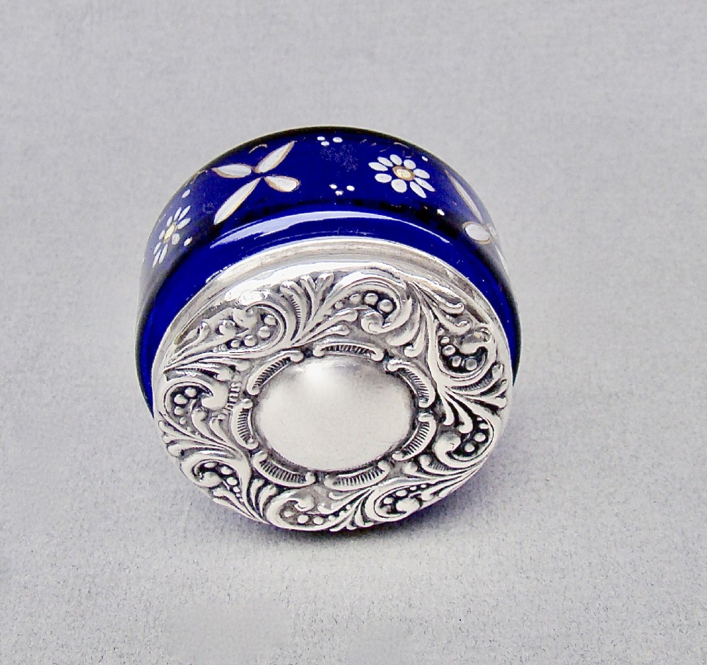 A small cylindrical cobalt blue glass jar decorated with white enamelled floral motifs and topped with an embossed silver lid. View III