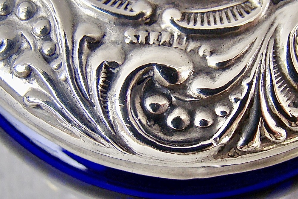 A small cylindrical cobalt blue glass jar decorated with white enamelled floral motifs and topped with an embossed silver lid. View IV
