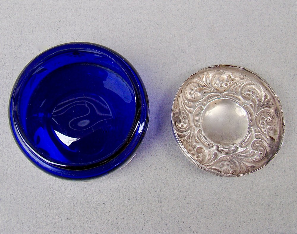 A small cylindrical cobalt blue glass jar decorated with white enamelled floral motifs and topped with an embossed silver lid. View V