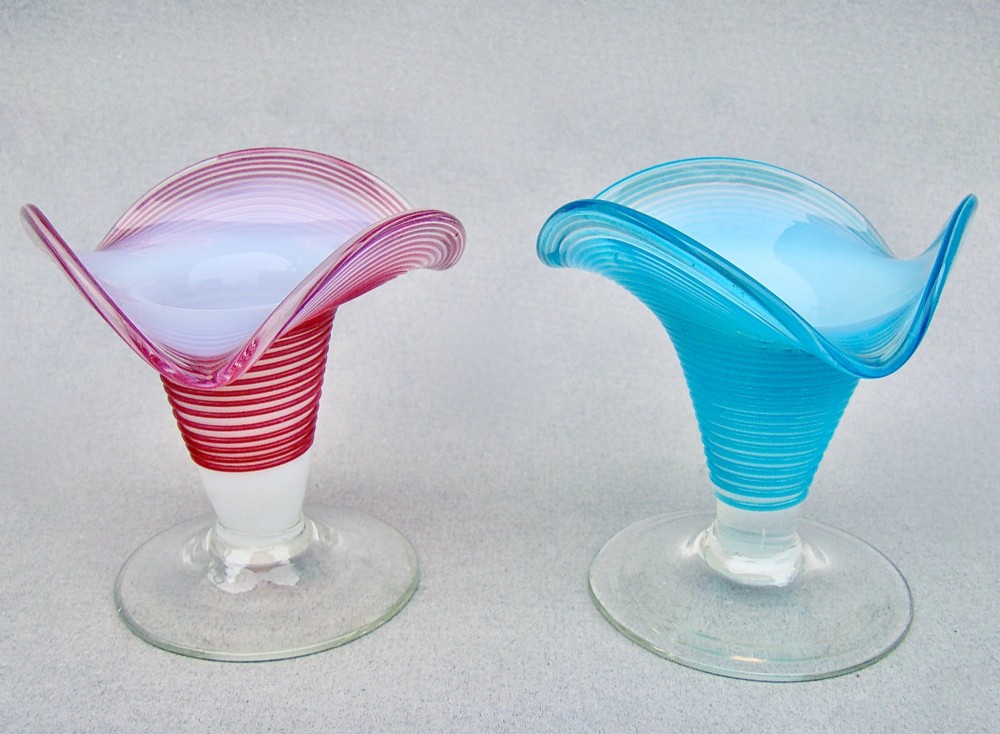 A pair of late Victorian opaline glass candlesticks with coiled threaded bodies and wide frilled rims, one in pink and one in turquoise blue.