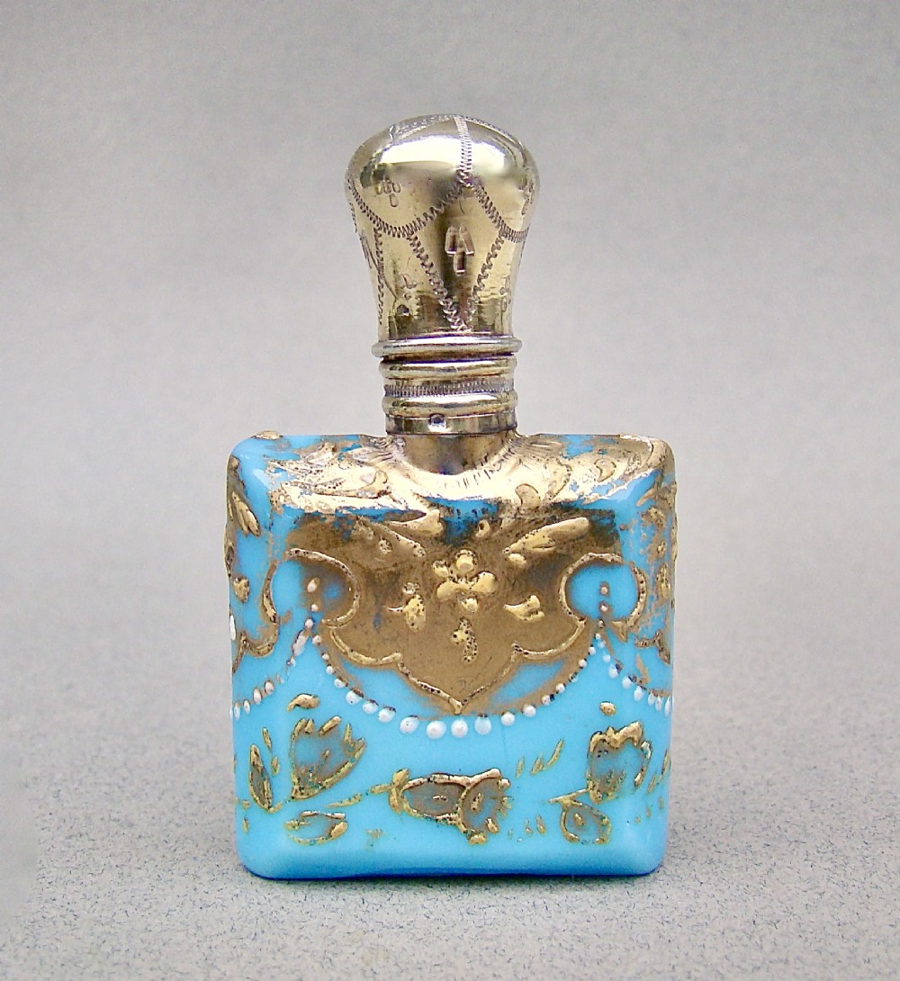 A small rectangular turquoise glass scent bottle featuring intricate gold scrollwork, white beaded enamel, and an engraved silver-gilt cap.