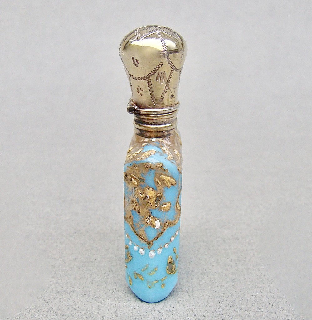 A small rectangular turquoise glass scent bottle featuring intricate gold scrollwork, white beaded enamel, and an engraved silver-gilt cap. View III