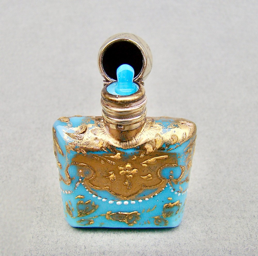 A small rectangular turquoise glass scent bottle featuring intricate gold scrollwork, white beaded enamel, and an engraved silver-gilt cap. View IV