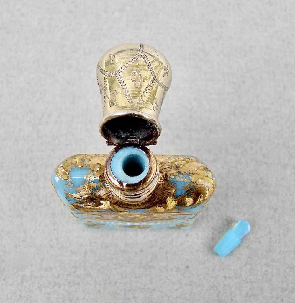 A small rectangular turquoise glass scent bottle featuring intricate gold scrollwork, white beaded enamel, and an engraved silver-gilt cap. View V