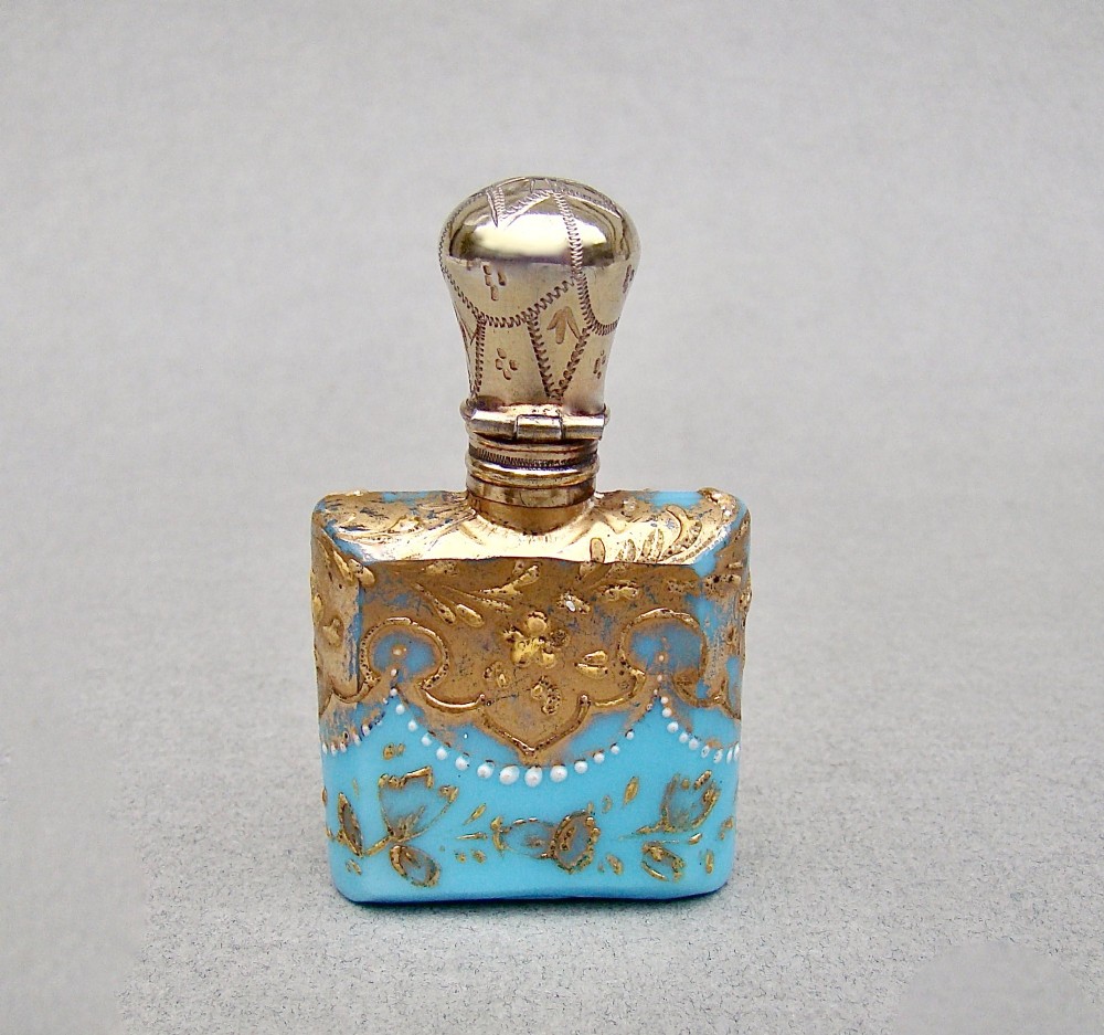 A small rectangular turquoise glass scent bottle featuring intricate gold scrollwork, white beaded enamel, and an engraved silver-gilt cap. View VI