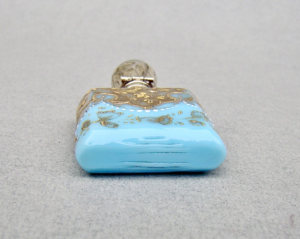 A small rectangular turquoise glass scent bottle featuring intricate gold scrollwork, white beaded enamel, and an engraved silver-gilt cap. View VIII