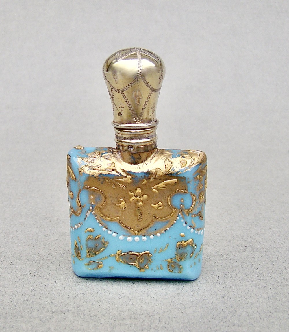A small rectangular turquoise glass scent bottle featuring intricate gold scrollwork, white beaded enamel, and an engraved silver-gilt cap. View IX