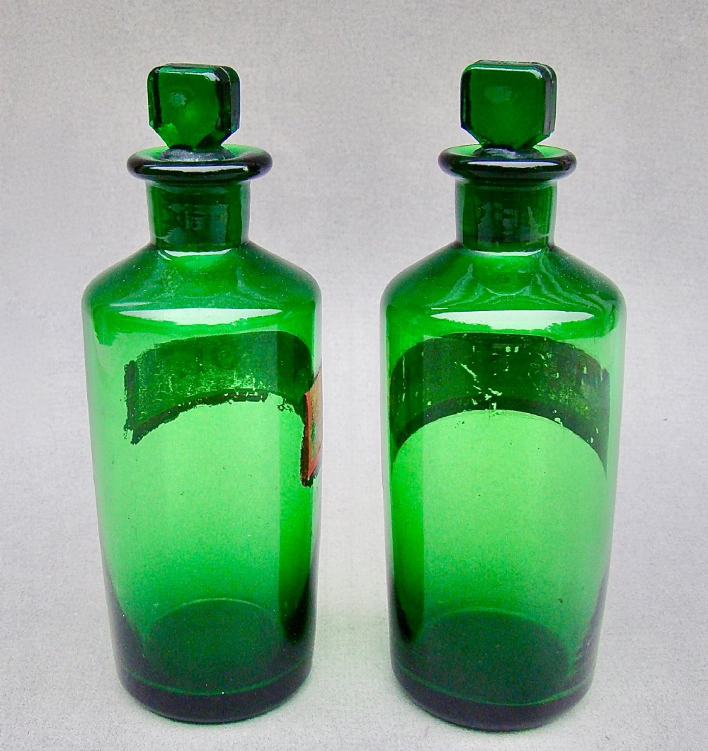 A pair of late Victorian cylindrical Bristol green glass apothecary bottles with ground stoppers and gilt-painted labels. View V