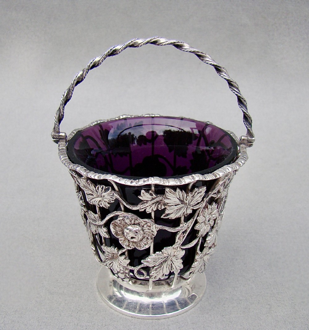 A sterling silver wirework sugar basket featuring a twisted swing handle, cast vine leaf motifs, and a removable purple glass liner. View II