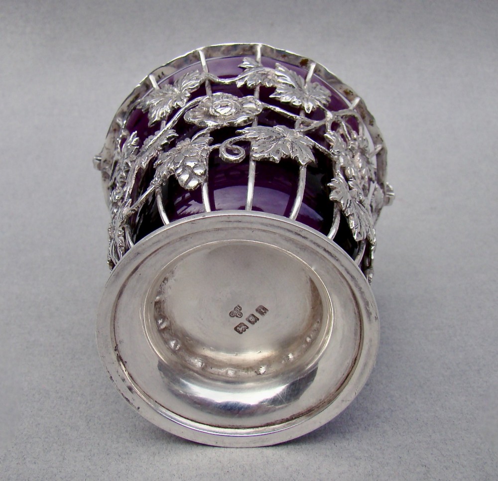 A sterling silver wirework sugar basket featuring a twisted swing handle, cast vine leaf motifs, and a removable purple glass liner. View V