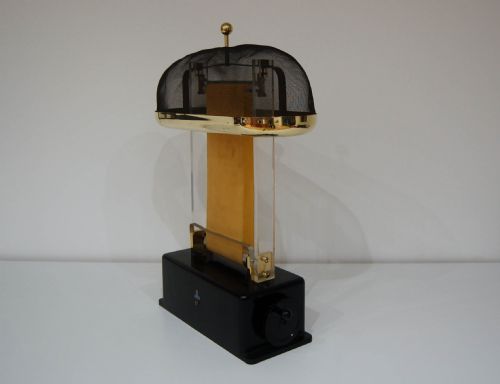 fig 1. A hand-cranked Van de Graaff electrostatic generator featuring a black metal base, transparent acrylic supports, an upright rubber belt, and a wire mesh upper dome trimmed in brass.