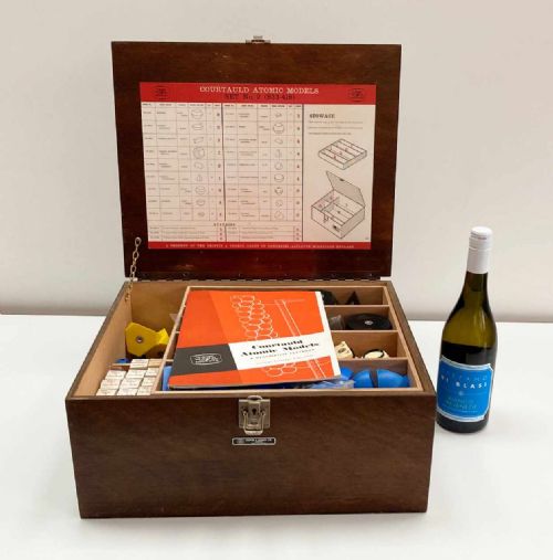 fig 1. A vintage wooden case filled with colourful plastic atomic model components, accompanied by an instructional booklet and a printed chart inside the lid.
