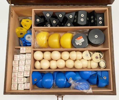 fig 3. A vintage wooden case filled with colourful plastic atomic model components, accompanied by an instructional booklet and a printed chart inside the lid.