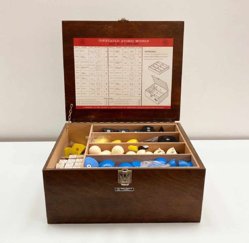 fig 4. A vintage wooden case filled with colourful plastic atomic model components, accompanied by an instructional booklet and a printed chart inside the lid.