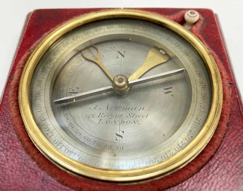 fig 2. A square red leather desk compass with a circular silvered dial, brass bezel, and a separate brass protective cap.