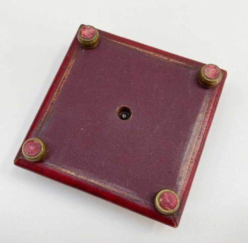 fig 3. A square red leather desk compass with a circular silvered dial, brass bezel, and a separate brass protective cap.