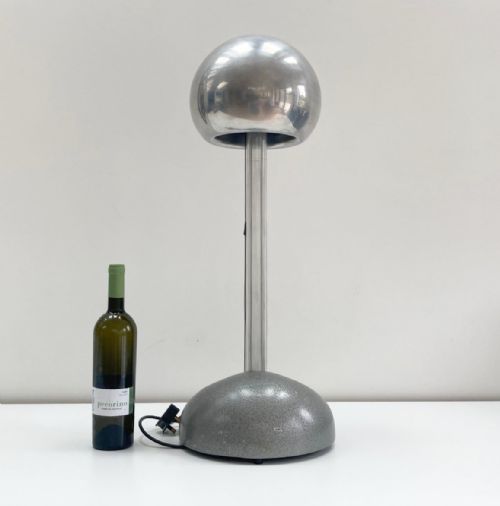 fig 1. A mid-twentieth-century Van de Graaff generator featuring a polished silver electrostatic sphere supported on vertical columns above a grey textured base, accompanied by a discharge wand with a wooden handle.