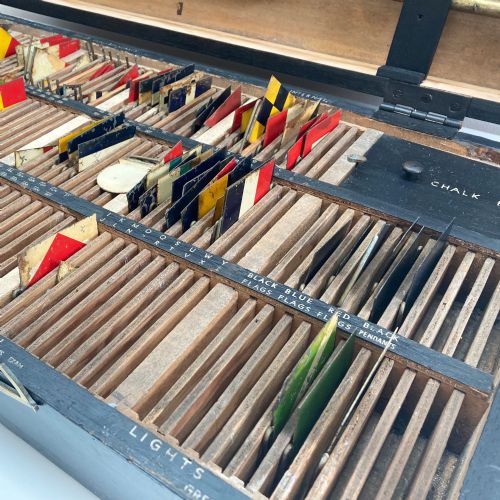 fig 3. An open early twentieth-century black wooden box featuring internal compartments with miniature signal flags and upright brass masts displaying colourful painted flags.