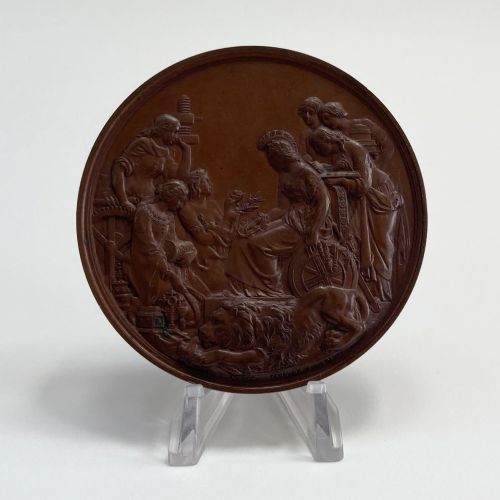 fig 2. A circular dark brown bronze medallion featuring high-relief classical allegorical figures surrounding a seated Britannia with a recumbent lion at her feet.