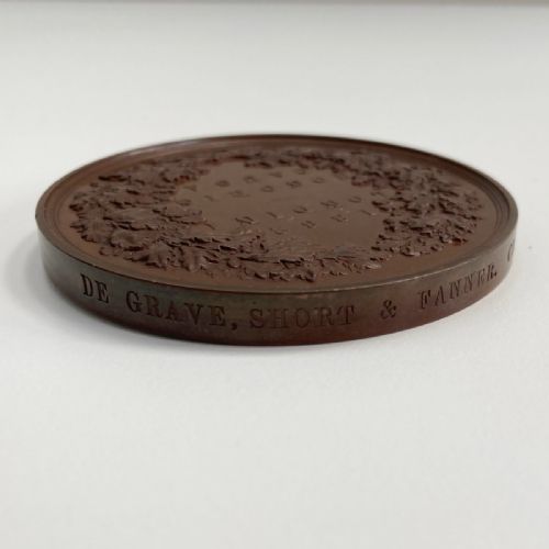 fig 4. A circular dark brown bronze medallion featuring high-relief classical allegorical figures surrounding a seated Britannia with a recumbent lion at her feet.