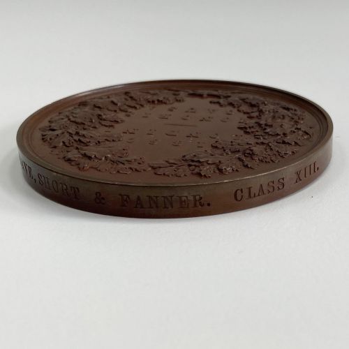 fig 5. A circular dark brown bronze medallion featuring high-relief classical allegorical figures surrounding a seated Britannia with a recumbent lion at her feet.