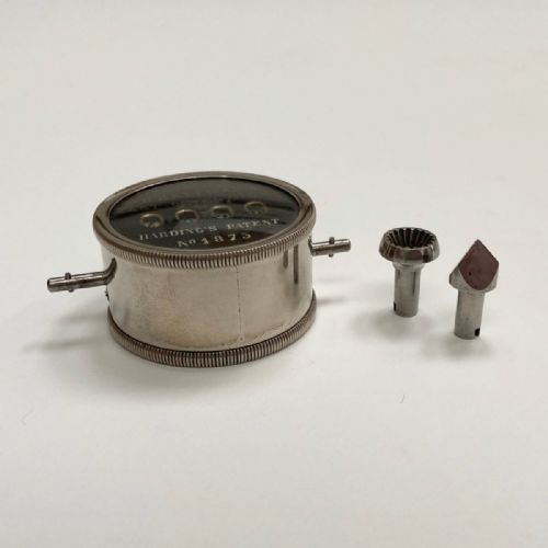 fig 2. A late Victorian pocket revolution counter made of nickel metal with a round glass face, resting inside its open original dark brown leather case lined with bright purple velvet.
