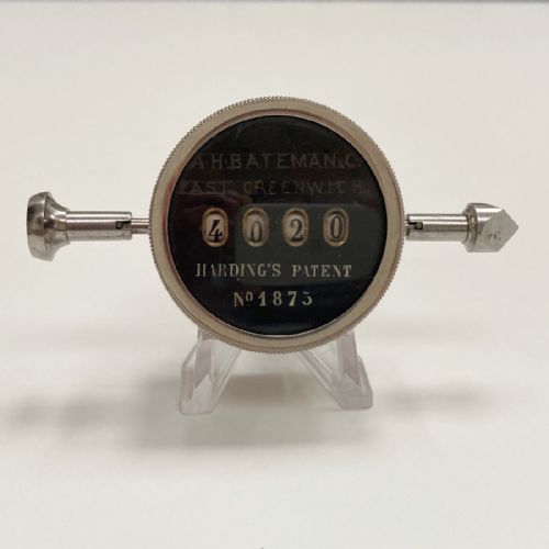 fig 4. A late Victorian pocket revolution counter made of nickel metal with a round glass face, resting inside its open original dark brown leather case lined with bright purple velvet.