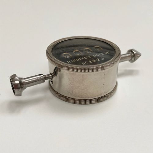 fig 5. A late Victorian pocket revolution counter made of nickel metal with a round glass face, resting inside its open original dark brown leather case lined with bright purple velvet.
