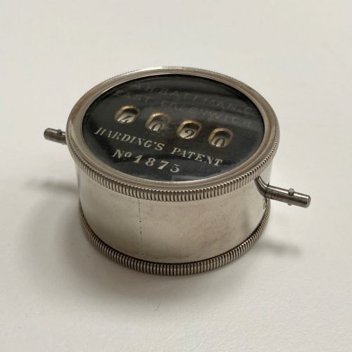 fig 6. A late Victorian pocket revolution counter made of nickel metal with a round glass face, resting inside its open original dark brown leather case lined with bright purple velvet.