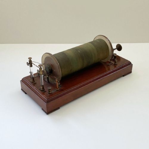 fig 3. An antique 19th-century Ruhmkorff induction coil featuring a central cloth-wrapped wire cylinder, brass fittings, glass discharge tubes, and a polished mahogany base.